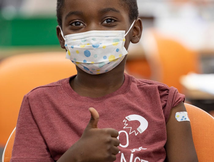 Young black boy with bandaid on shoulder makes thumbs up gesture.