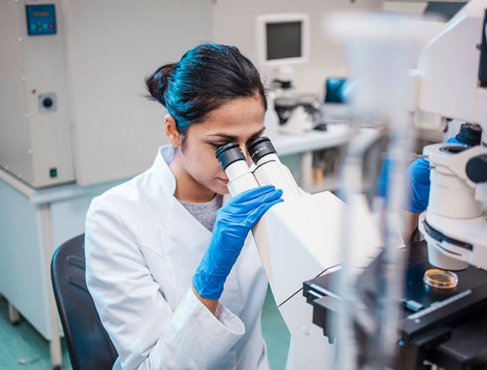 A female researcher in a lab peers into a microscrope