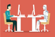 human sitting at computer across from robot sitting at computer