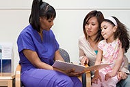 It’s Time to Get Back to the Basics On Social Determinants. A clinician reads a brochure with a mother and her daughter.