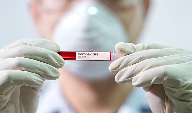 Hospitals Prepare for Influx of Patients with Coronavirus. A clinician in a mask and gloves hold a vial with blood in it labeled Coronavirus.