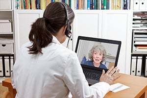 Coronavirus COVID-19 Telehealth and Virtual Care. A clinician with a headset on talks through her  on a laptop computer to a remote patient at home via telehealth.