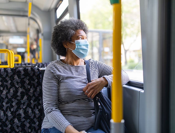 Lady sitting on bus looking out window with mask on