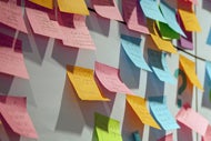 Intermountain Healthcare CEO Shares Takeaways from COVID-19. Many different colored Post-It notes with writing on them stuck on a white board.