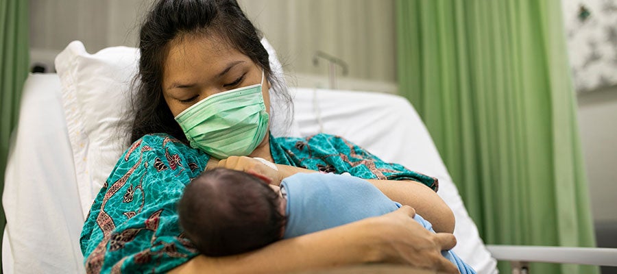 Mother in hospital bed, wearing mask and holding newborn baby