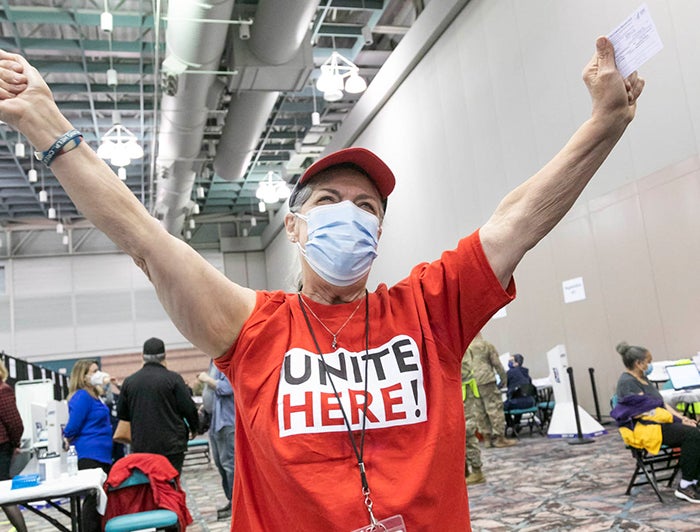 masked woman at vaccine event stands with arms raised in celebration