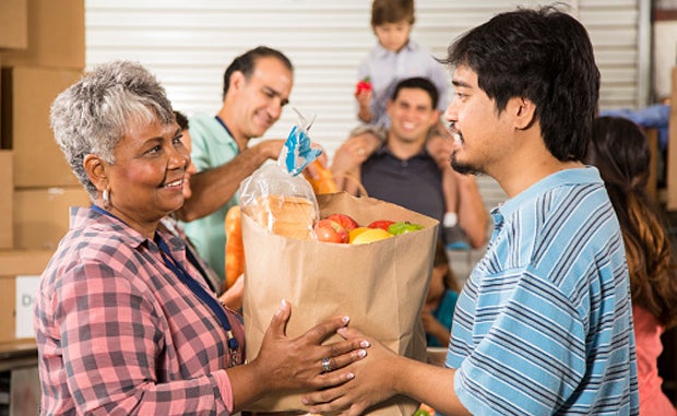 3 Keys to Meet Individuals’ Health and Social Needs. A Latino man hands a bag of groceries to a Black woman.