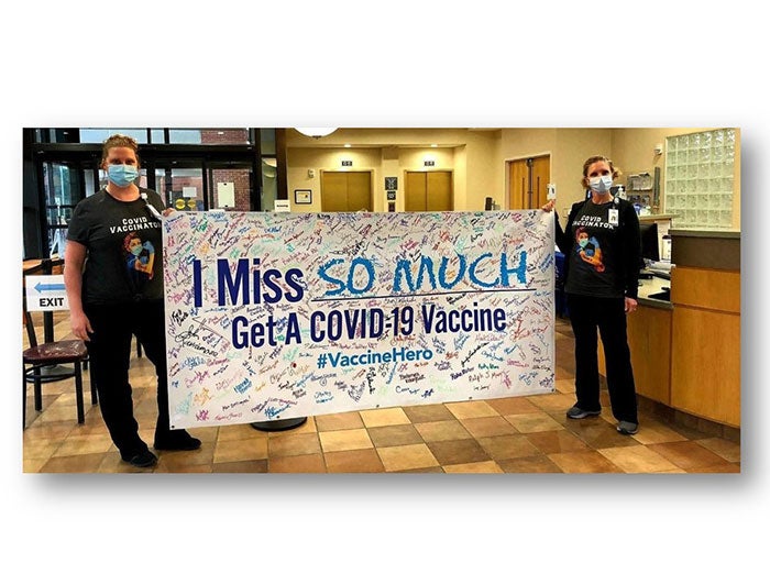 Lifepoint health workers hold up sign saying 'I Miss: So Much'. Get a COVID-19 Vaccine #VaccineHero .