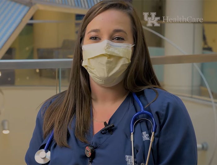 UK HealthCare worker wearing scrubs and mask discusses her patients