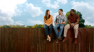 A woman and two men sit talking atop a wooden fence