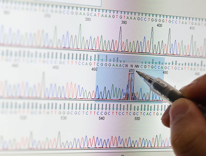 Computerized graph of gene sequenced code being pointed at with hand holding a pen