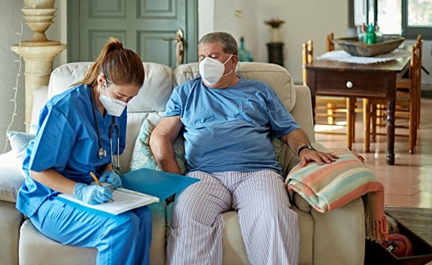 Health Systems Forge Partnerships to Bring Hospital-Level Care to the Home. A clinician wearing a mask fill out a form with a patient wearing a mask in the patient's house.