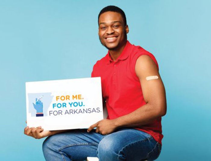 Baptist health poster shows black man with bandaid on bicep, holding sign that says For You. For Me. For Arkansas.