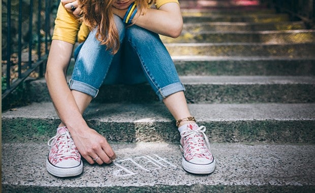 3 Steps to Take When Assessing Virtual Mental Health. A women suffering from mental health issues sits on the steps of a brownstone and writes HELP on the bottom stair in chalk.