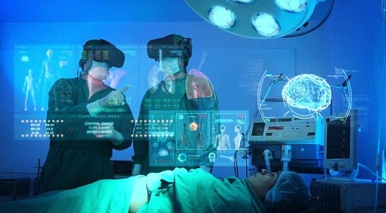 How Wearable Cognitive Assistance Tools Could Reshape Care Delivery. Two clinicians in surgery look at a heads-up display of medical information on the patient who is lying on an operating table.