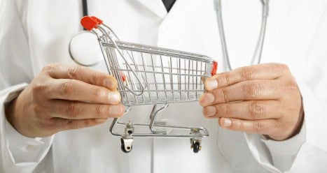 Instacart Puts Groceries and Health Care into One Basket. A physician in a white lab coat with a stethoscope around his neck holds a small metal shopping cart.