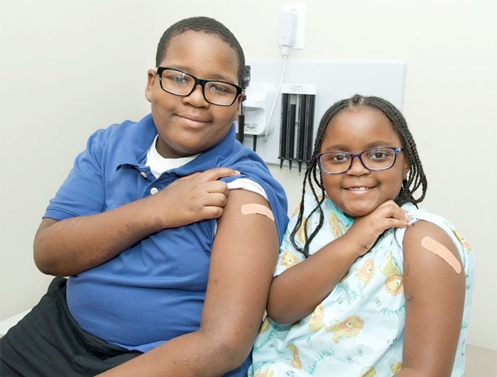 Young black boy and girl show off arms with bandaids on them after vaccination.