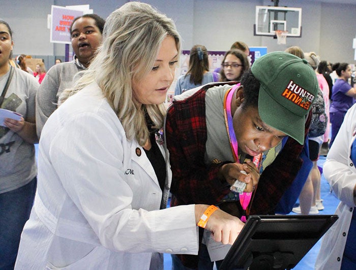 Health care worker stands with patient starting at glowing screen
