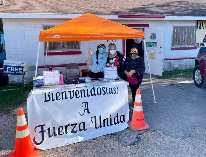 Three women stand at Bienvenidos a Fuerza Unida tent