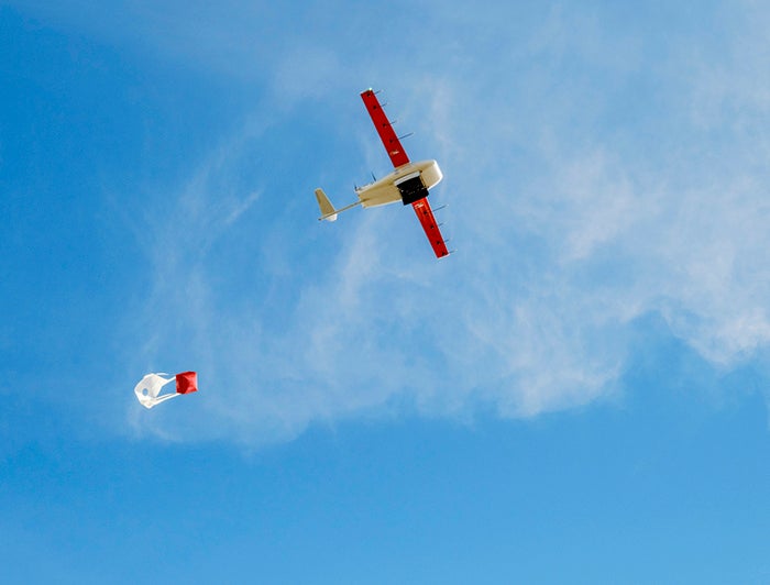 Zipline drone flies across blue sky trailing a package for delivery