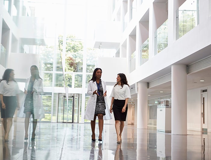 female physician and female executive have walking meeting in hospital atrium