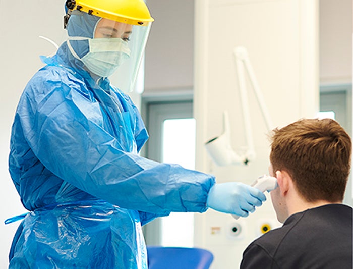 Stock Photo of health worker in full PPE taking patient's temperature in triage bay