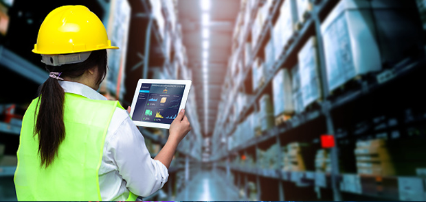High-Performing Supply Chain Leaders to Share Insights on Improving Resiliency. A warehouse worker in a hardhat and reflective vest holds a tablet while checking inventory.