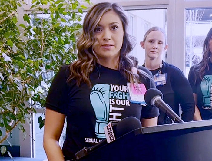 Woman stands at a podium wearing tee that reads Your Fight is Our Fight