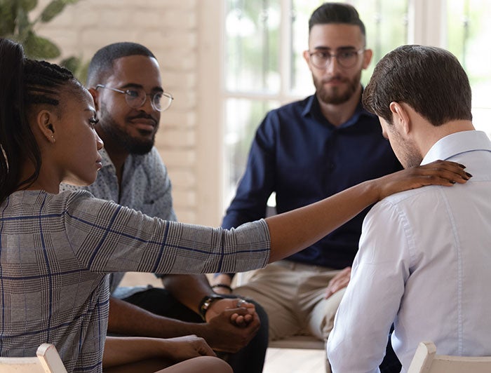Stock photo of three diverse men sitting with a Black female counselor in a group therapy session