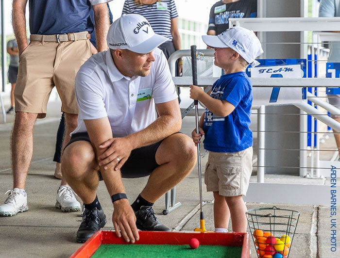 A young patient gets a tip from his caddy, who is crouched at eye level to the child