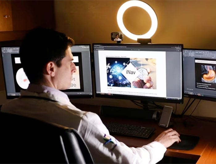 photo of oncologist using iNav on a computer with three montitors and a ring light