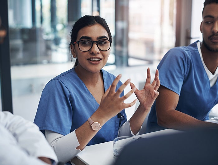 Stock photo of female health worker in glasses and scrubs talking to colleagues