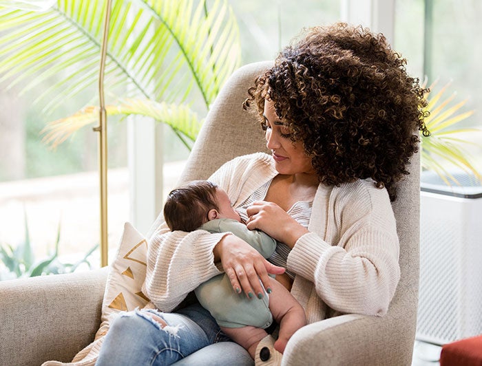 Curly haired young mother sits in an armchair while nursing her baby