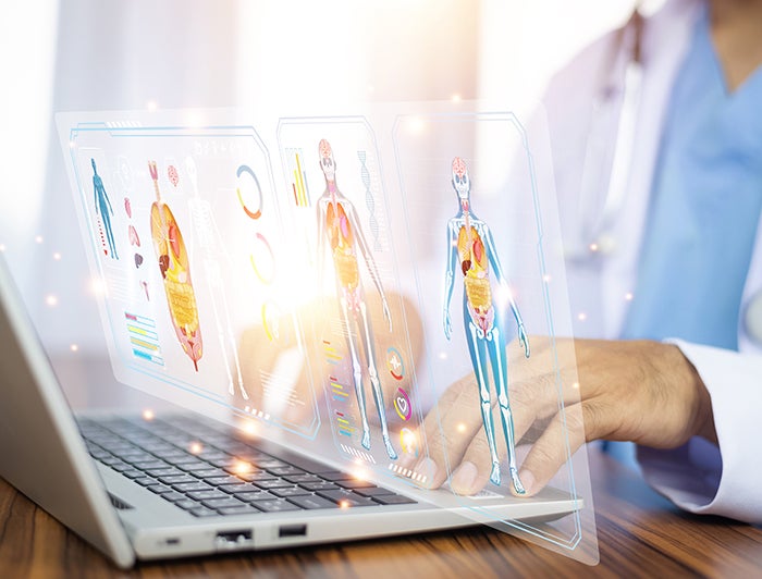 Hartford HealthCare. Stock photo of health worker in white coat seated with laptop computer with hologram of human anatomy over keys