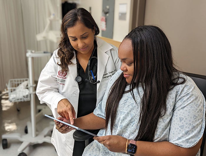 Loma Linda University Medical Center - Female LLUMC clinician stands and reviews a tablet with a female ER patient in hospital gown
