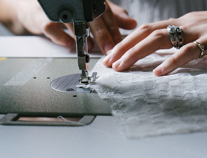 University of Michigan Health. Hands guide wedding dress fabric through a sewing machine