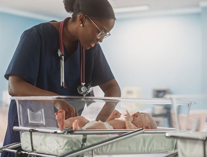 Childrens Hospital Colorado, Ivinson Memorial Hospital. Stock image of a Black female clinician comforting a newborn in bassinet