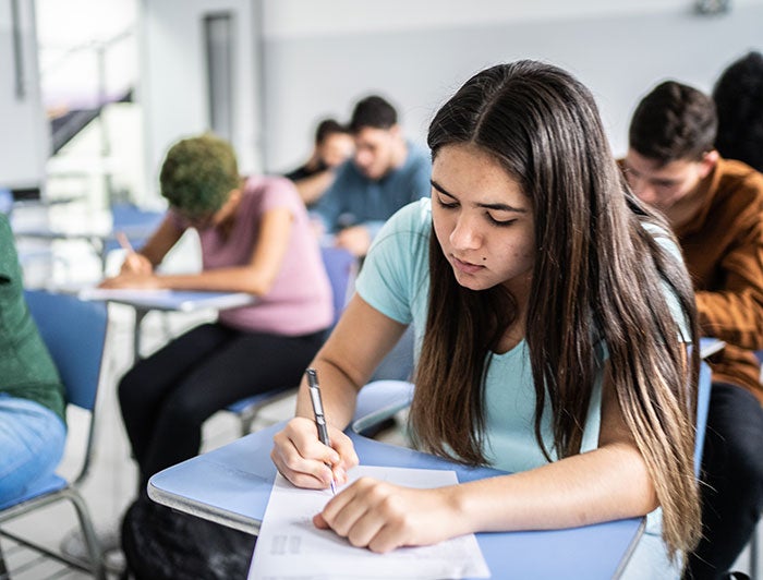 Newton-Wellesley Hospital. Photo of a young woman seated at a desk taking a test among rows of other students doing the same