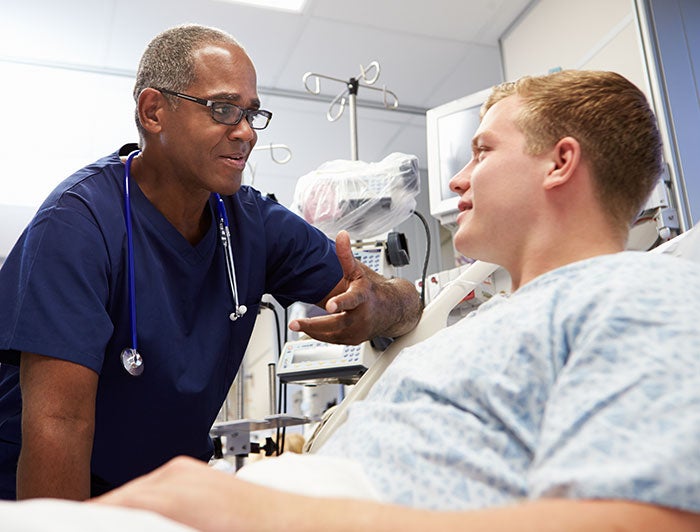 Saline Memorial Hospital. Male Clinician sits bedside talking to a male patient in a hospital bed