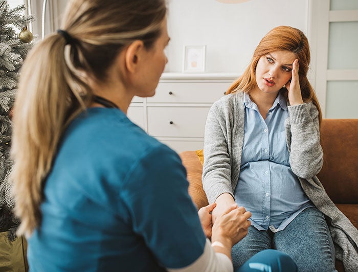 Woman’s Hospital. Pregnant woman sits talking with a female clinician