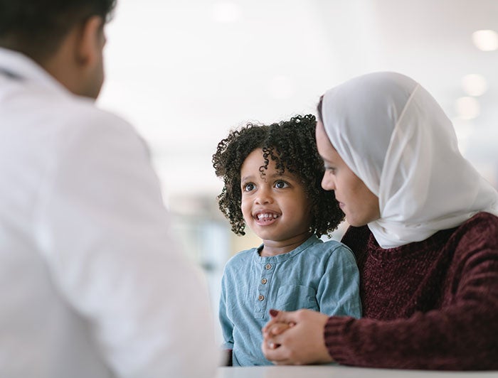 Texas Children's Hospital. A smiling, curly haired child and mother in head scarf sit talking to a white coated physician