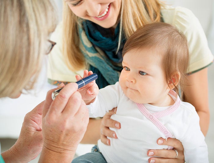 A baby stares at a pen held in front of her face by a female physician