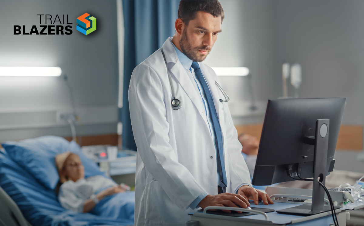 4 Steps to Deliver Real-Time Health Data at the Point of Care. A physician in a patient's room enters real-time health data at the point of care into a computer.
