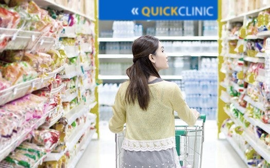 4 Takeaways from Survey on Retail Health Clinics and Quality. An Asian woman walks down a grocery store aisle with a Quick Clinic sign at the end of the aisle.