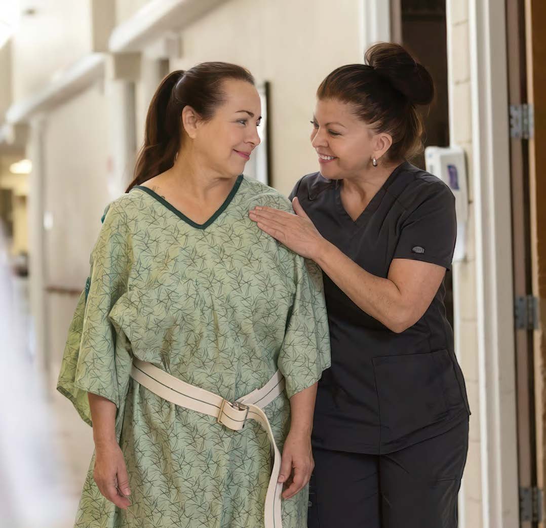 A patient in hospital gown and wearing a support belt at ScionHealth does PT in a hospital hallway with the help of a clinician.