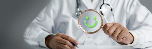 Success Stories in Driving Quality and Safety Improvement. A physician takes notes while looking through a magnifying glass with a green smile icon on it.