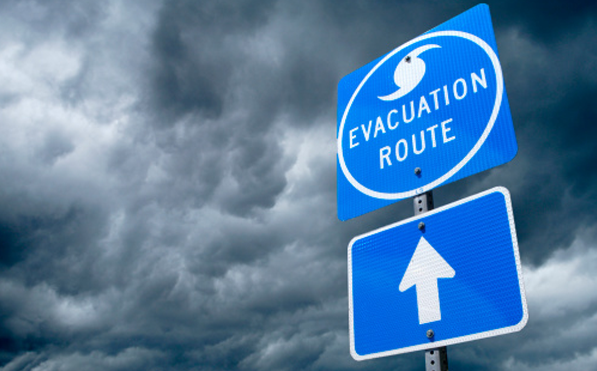 Top Priority — 3 Health Care Emergency Preparedness Tips. A blue hurricane evacuation route sign with storm clouds in the background.