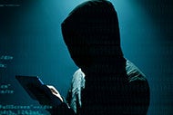Intellectual Property Theft: A Growing Threat to Research and Innovation. Image of a hacker with his face hidden in a hoodie working on breaking into a website.