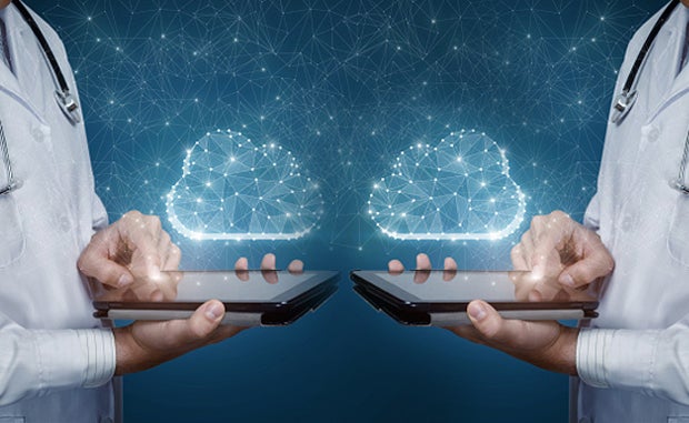 Digital Transformation’s Next Wave: Creating a Mirrored World. Mirror images of two doctors with tablets in their hands facing each other and sharing data in the cloud.