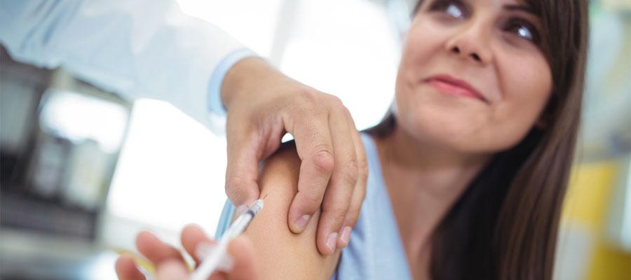 A clinician delivers a flu vaccine into a female patient's right arm.
